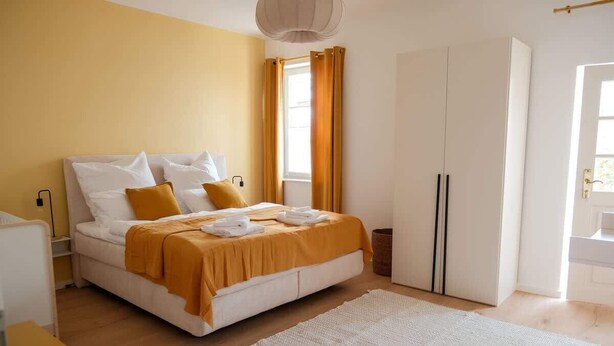 Ein Schlafzimmer mit Bett, Kleiderschrank, Nachttisch und einem Fenster mit Vorhängen.