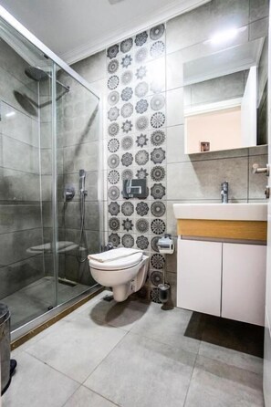 A bathroom with a shower, toilet, sink, and patterned tiles. - m2 otel (Bodrum)