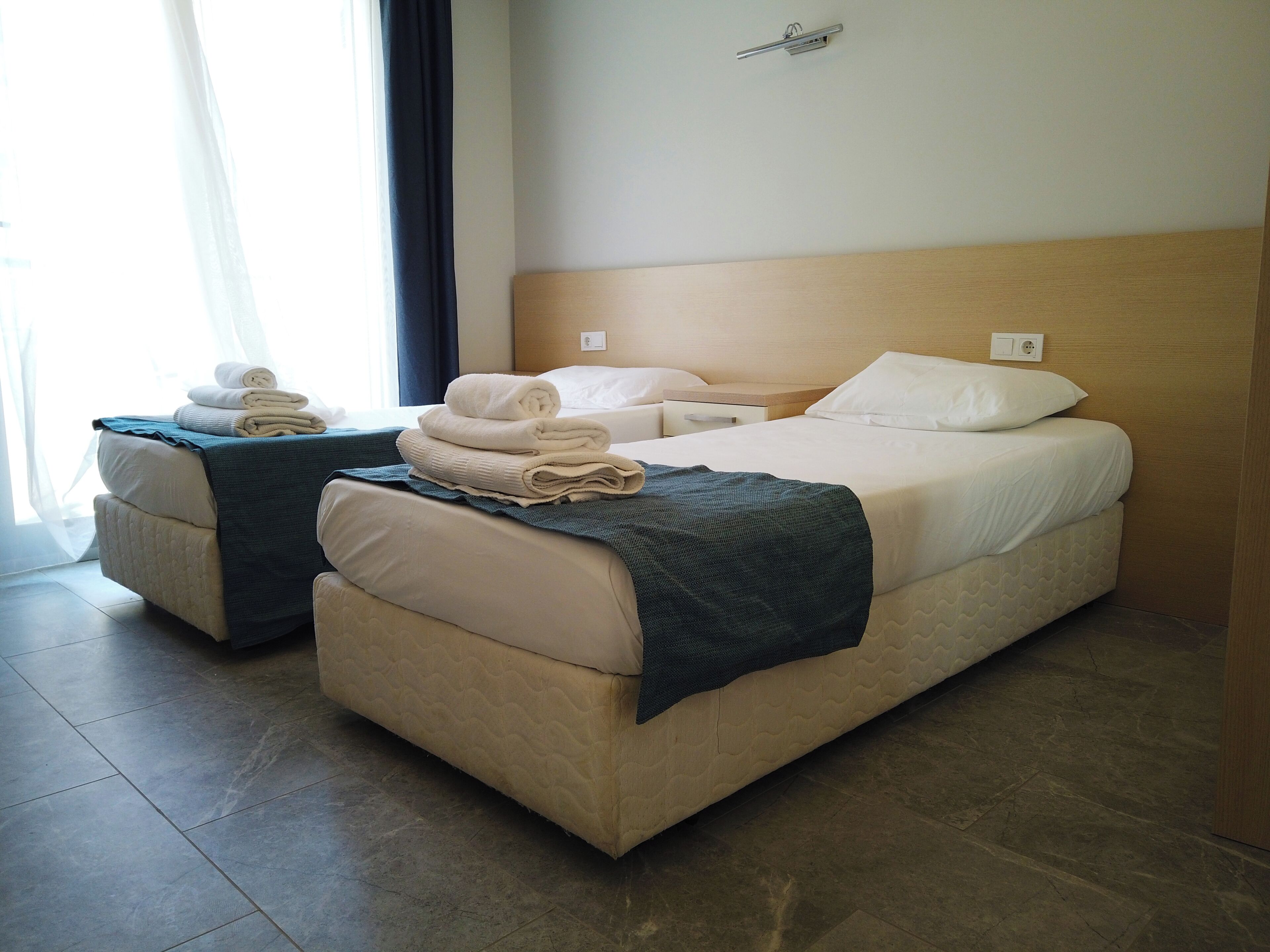 Ein Hotelzimmer mit zwei Betten, einem Kopfteil, einem Nachttisch und einem Fenster mit Vorhängen.