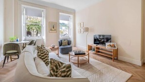 A living room with a sofa, armchair, and a television on a stand. - Elegant 1-Bedroom apartment in Bath - VAT Q (Bath)