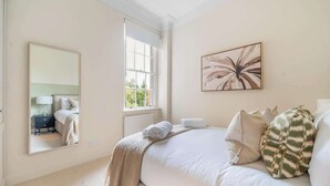 A bedroom with a large bed, a window, a mirror, and a wall-mounted artwork. - Elegant 1-Bedroom apartment in Bath - VAT Q (Bath)