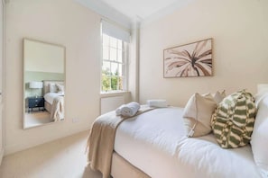 A bedroom with a large bed, a window, a mirror, and a wall-mounted artwork. - Elegant 1-Bedroom apartment in Bath - VAT Q (Bath)