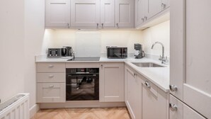 A compact kitchen with a built-in oven, a microwave, a coffee maker, and a sink. - Elegant 1-Bedroom apartment in Bath - VAT Q (Bath)