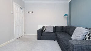 Um quarto com um sofá cinzento, um radiador branco, um candeeiro de chão azul-turquesa e uma porta branca.