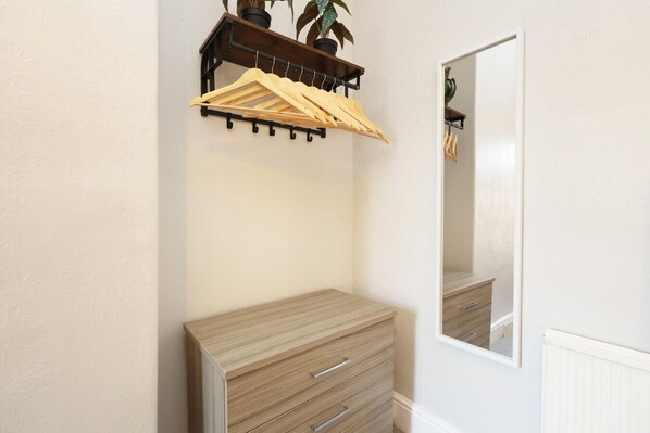 A room with a wooden dresser, a mirror, and a wooden clothes rack with hangers.