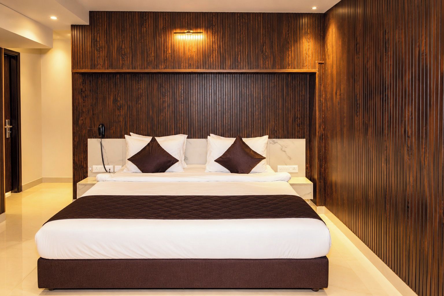 Une chambre à coucher moderne avec un grand lit, des panneaux de bois au mur et une table de chevet avec une lampe.
