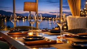 A dining table set with wine glasses, plates, and a candle, overlooking a body of water and mountains. - Shakuntalam Sagar - Luxury Boutique Lake View Hotel, Udaipur (Udaipur)
