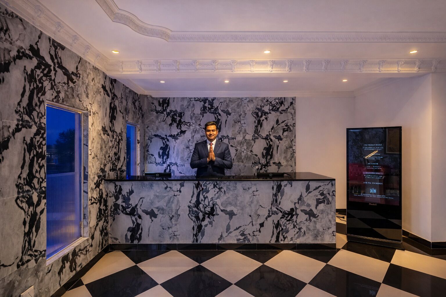 A reception desk with a marble wall, a checkered floor, and a large screen displaying information.