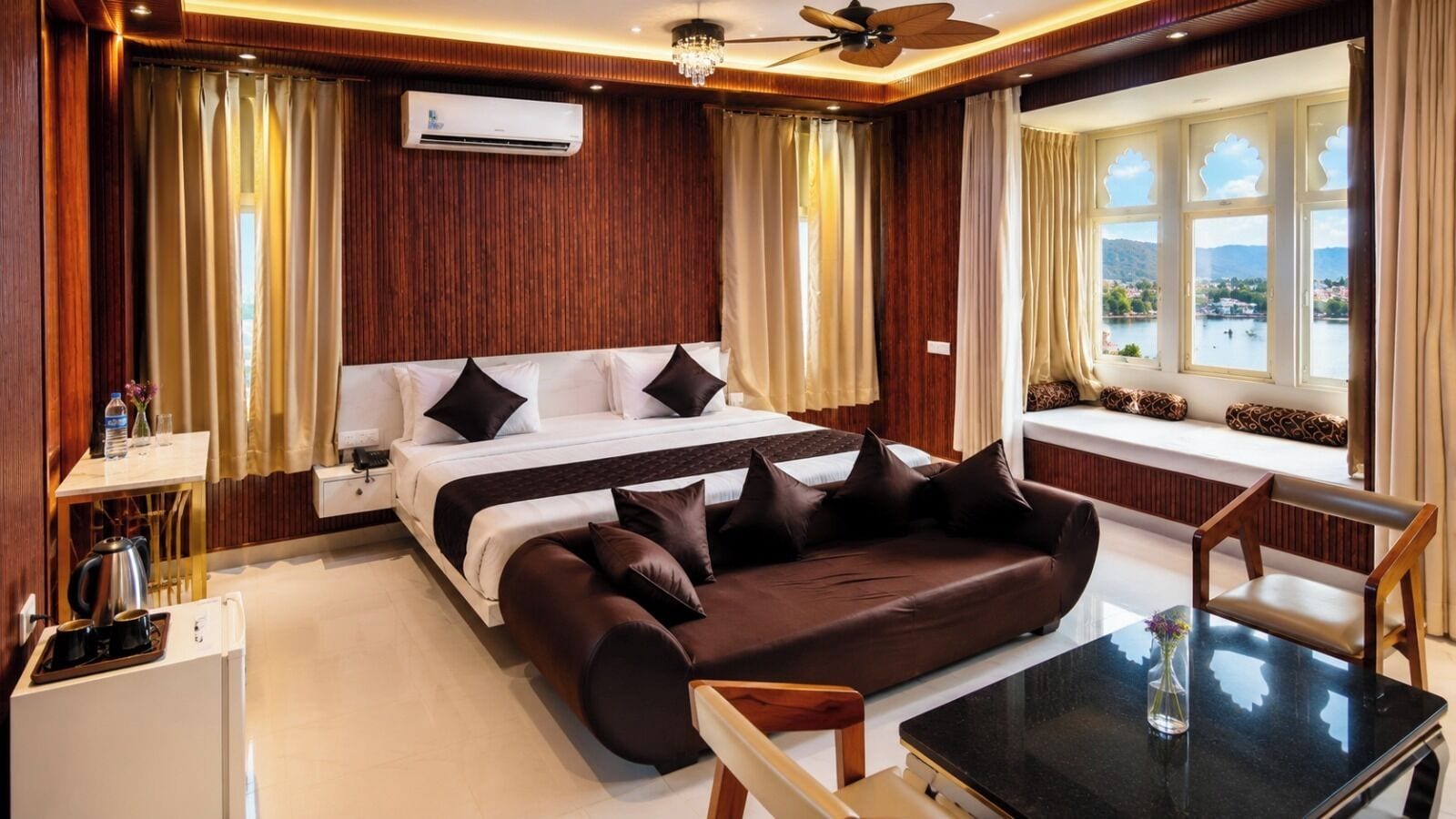 A hotel room with a bed, a sofa, a dining table, and a view of a lake.