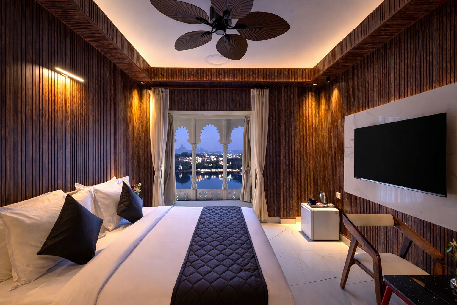 Habitación de hotel con una cama grande, televisión, ventilador de techo y vistas a la ciudad.