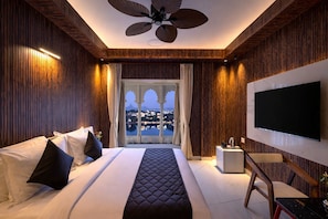A hotel room with a large bed, a TV, a ceiling fan, and a view of a cityscape. - Shakuntalam Sagar - Luxury Boutique Lake View Hotel, Udaipur (Udaipur)