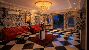 A luxurious living room with a checkered floor, red sofas, a chandelier, and a large window. - Shakuntalam Sagar - Luxury Boutique Lake View Hotel, Udaipur (Udaipur)