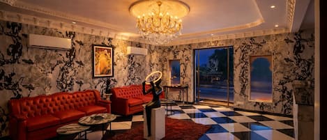 A luxurious living room with a checkered floor, red sofas, a chandelier, and a large window.