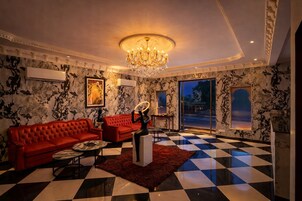 Una sala de estar lujosa con piso a cuadros, sofás rojos, una araña de cristal y un ventanal grande.