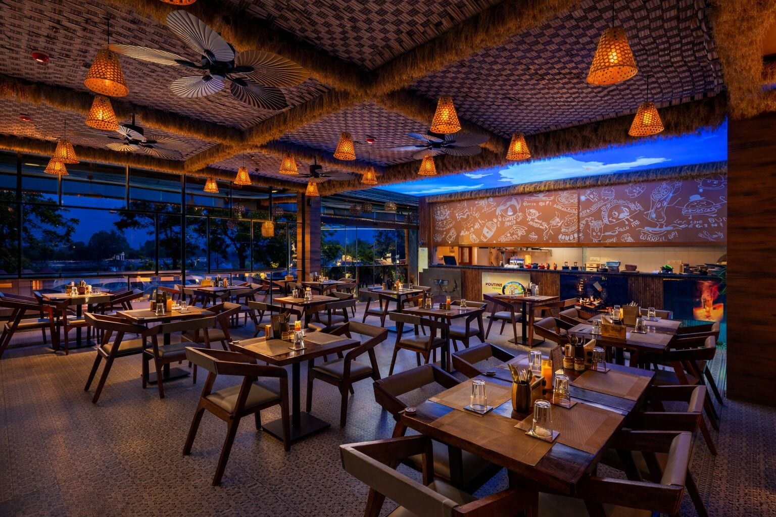 Um restaurante com várias mesas e cadeiras, ventiladores de teto e luminárias pendentes.