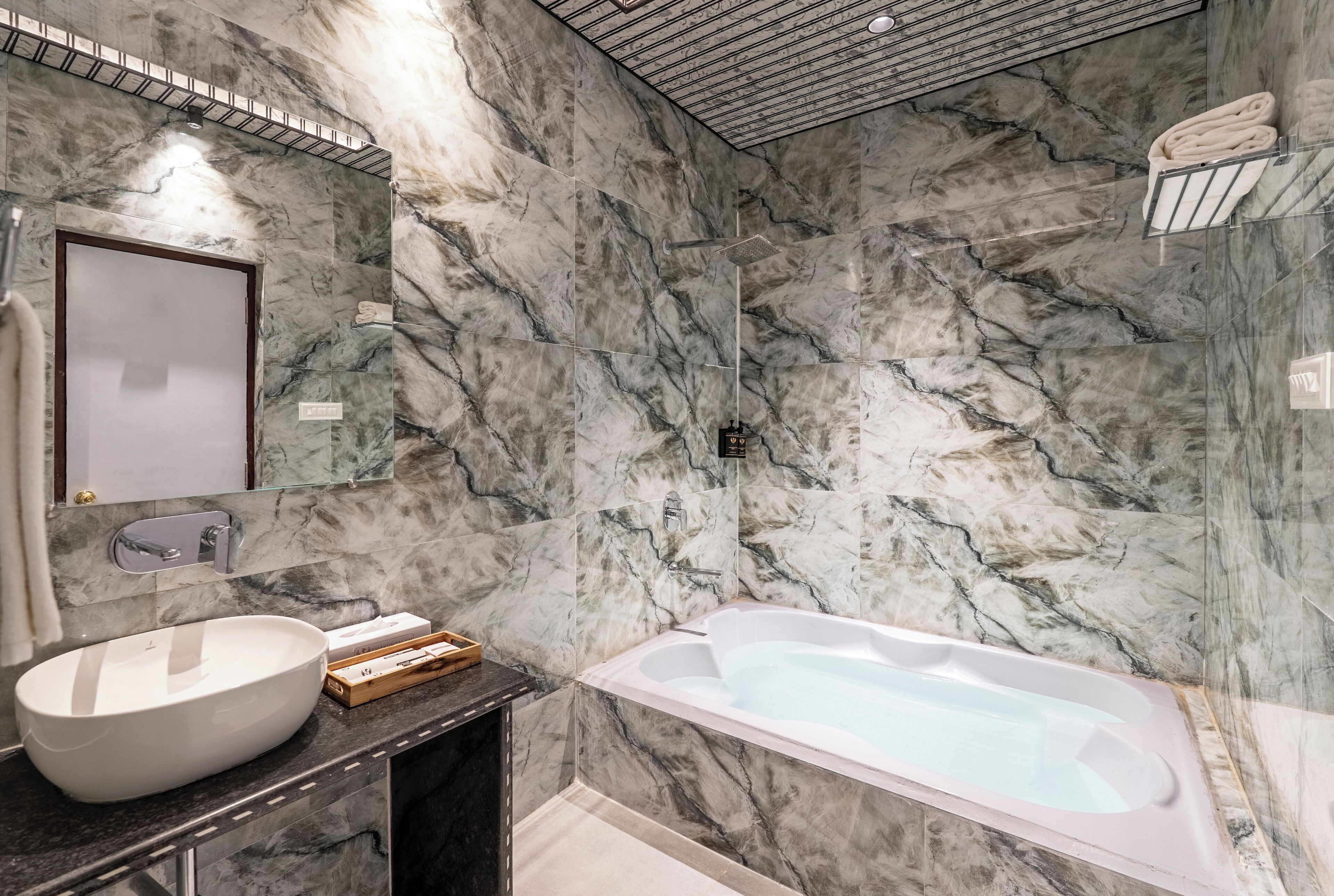 A bathroom with a marble wall, a white sink, a bathtub, and a towel rack.
