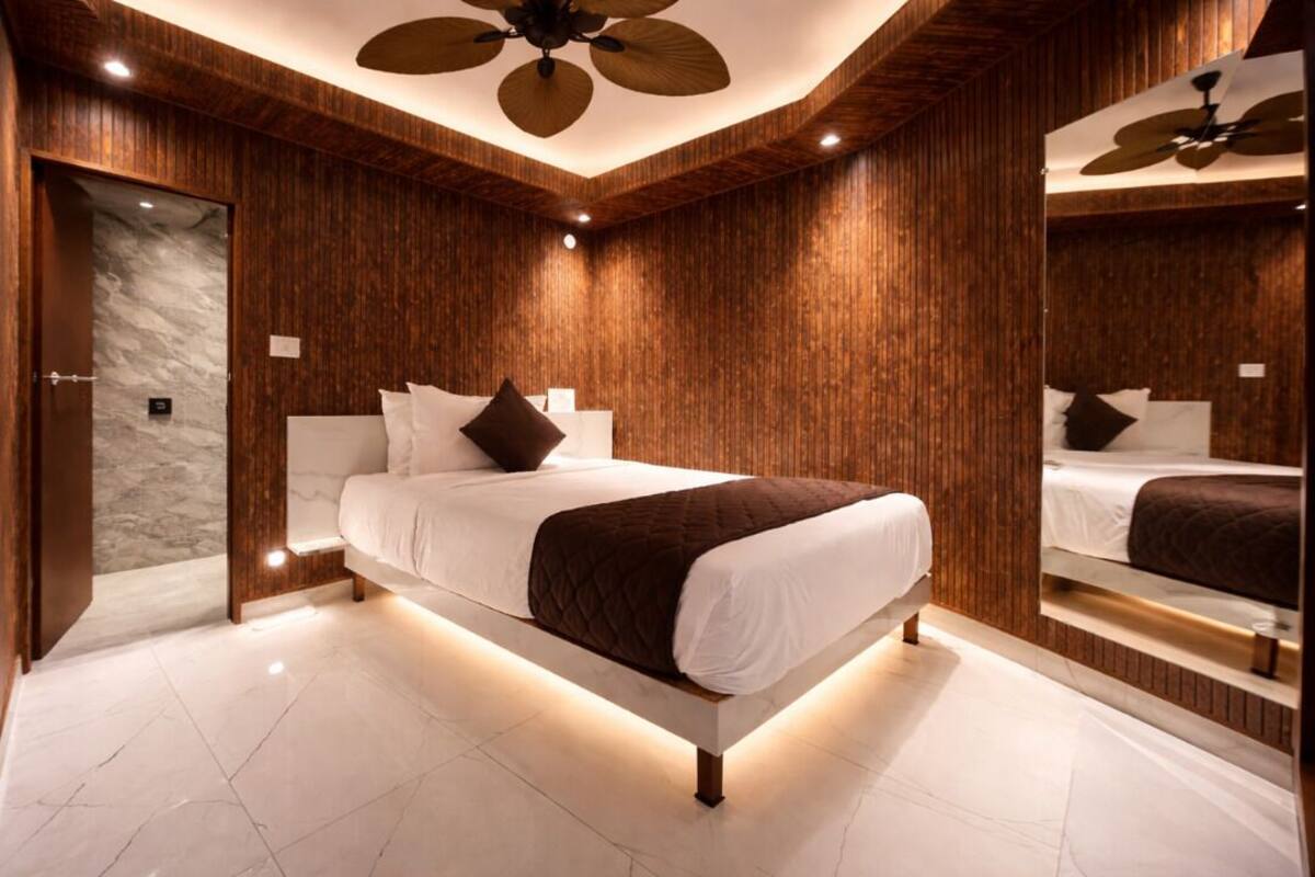 Un dormitorio moderno con una cama grande, paneles de madera, un ventilador de techo y suelo de mármol.