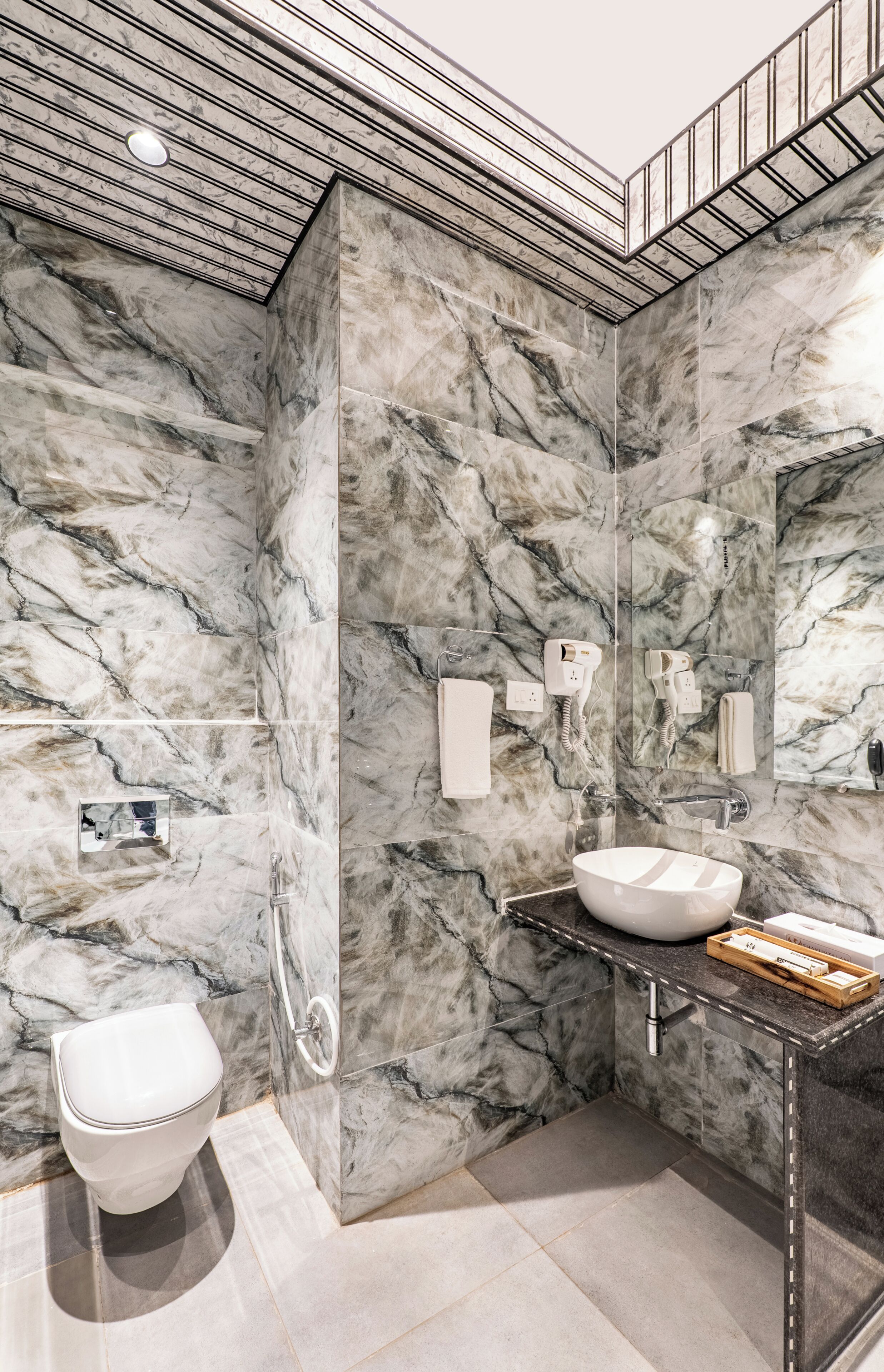 Un baño moderno con paredes de mármol, inodoro blanco, lavamanos con encimera de mármol y zona de ducha.