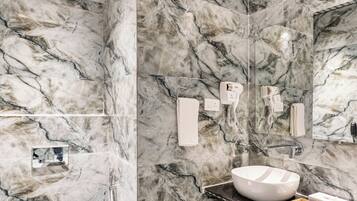 A modern bathroom with marble walls, a white toilet, a sink with a marble countertop, and a shower area.