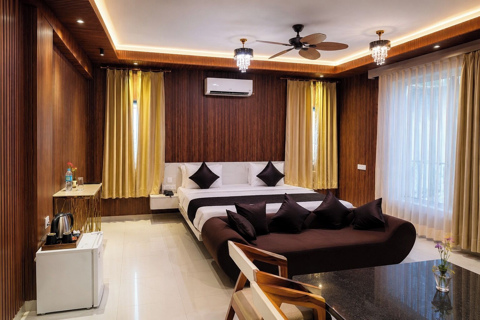 A hotel room with a bed, a sofa, a coffee table, a desk, and a ceiling fan.