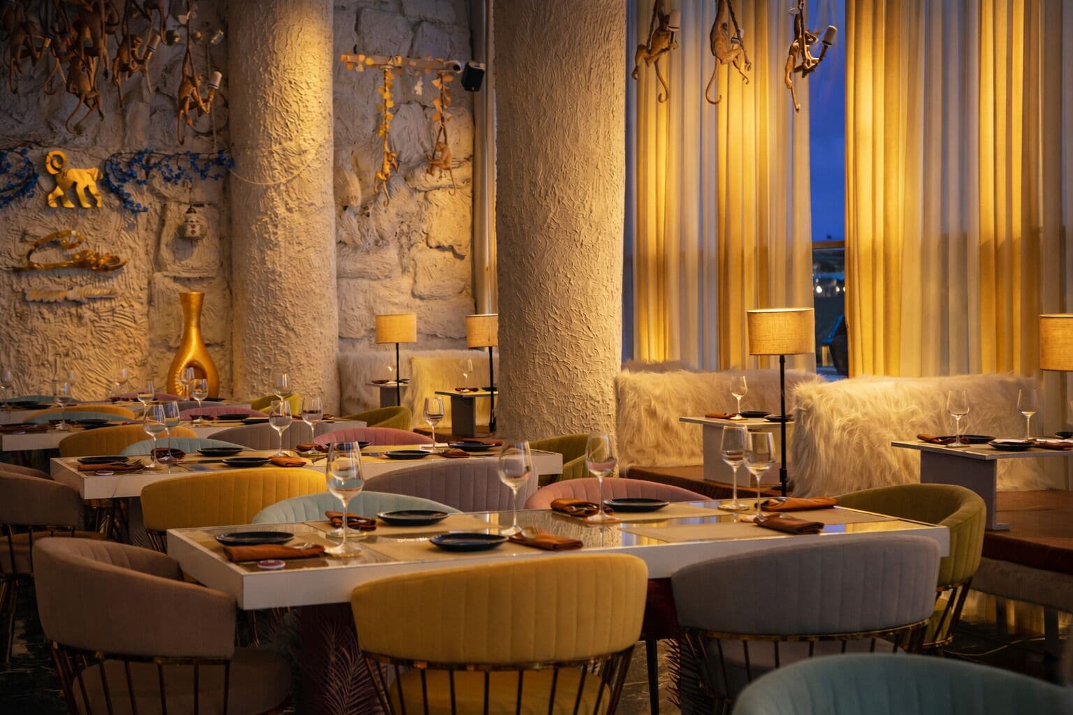 A restaurant with tables set for dining, a stone wall, and hanging decorations.