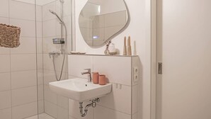 Ein Badezimmer mit Dusche, Waschbecken, Spiegel und Pflegeprodukten.