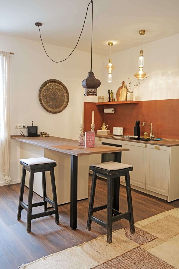 A kitchen with a wooden island, two stools, pendant lights, a decorative plate, and a sign.