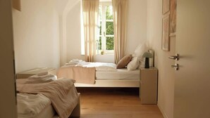 A bedroom with a bed, a bedside table, a lamp, a window with curtains, and a door.