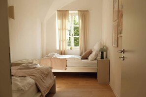 Un dormitorio con cama, mesita de noche, lámpara, ventana con cortinas y puerta.