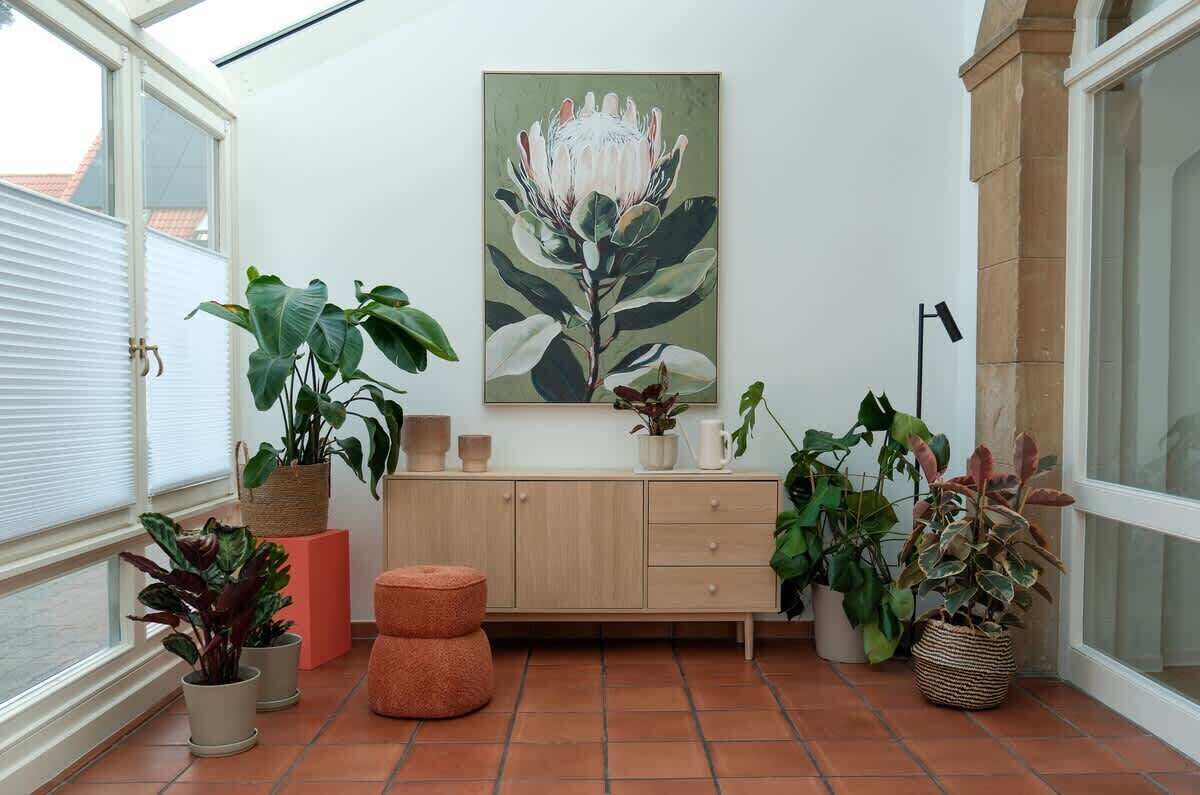 Une véranda avec un banc en bois, des plantes en pot et un tableau accroché au mur.