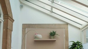 A conservatory with a table and chairs, a potted plant, and a small shelf with decorative items.