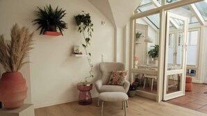 A room with a large window, a chair, a table, and various plants.