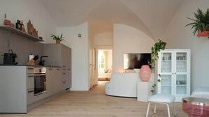 A modern kitchen with built-in appliances, a dining area with a white table and chair, and a living room with a sofa and TV.