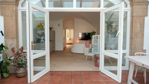An open doorway leading to a living area with a TV, seating, and potted plants.