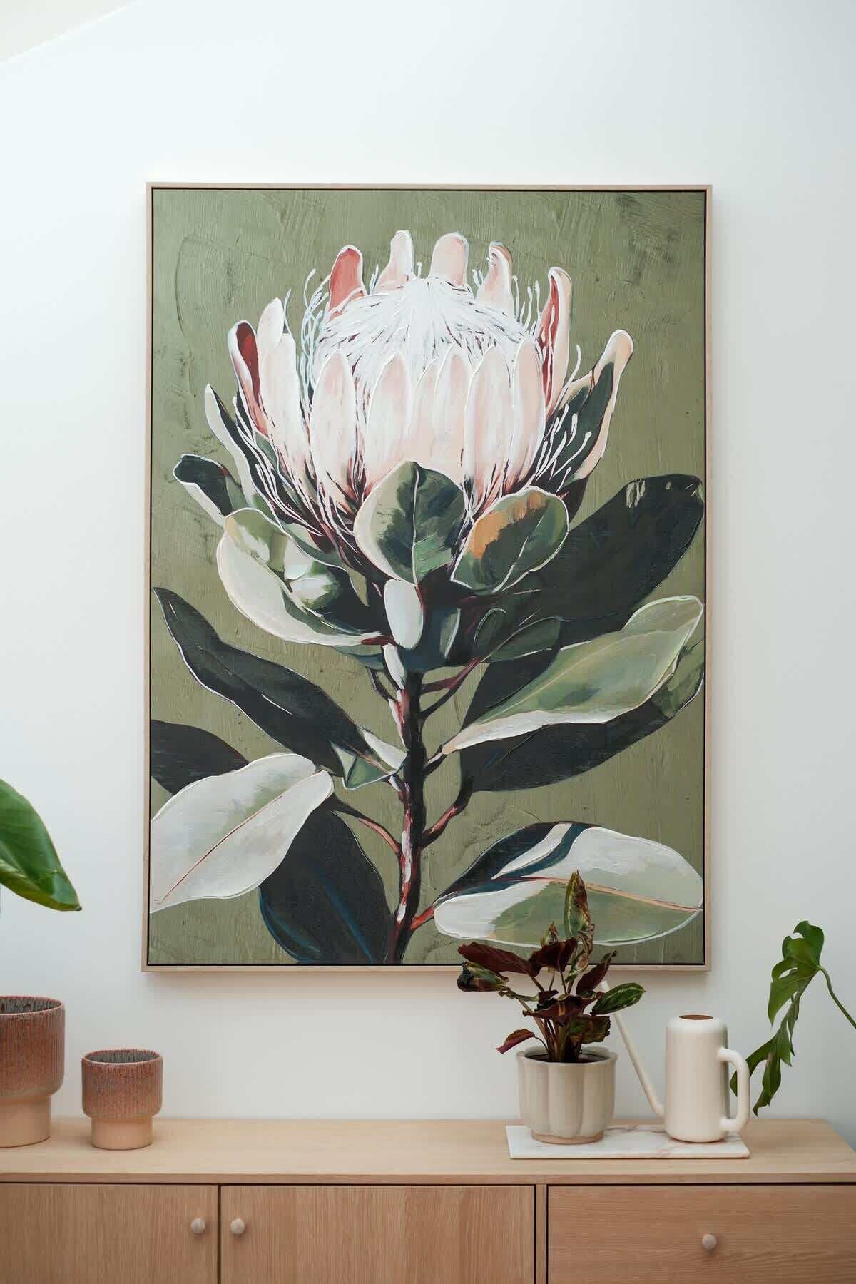 Ein gerahmtes Bild von einer weißen Blume mit grünen Blättern an einer Wand.
