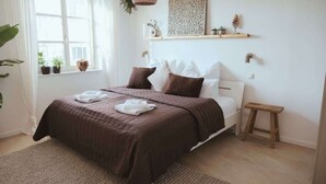 Quarto com cama, mesa de cabeceira, janela e objetos decorativos.