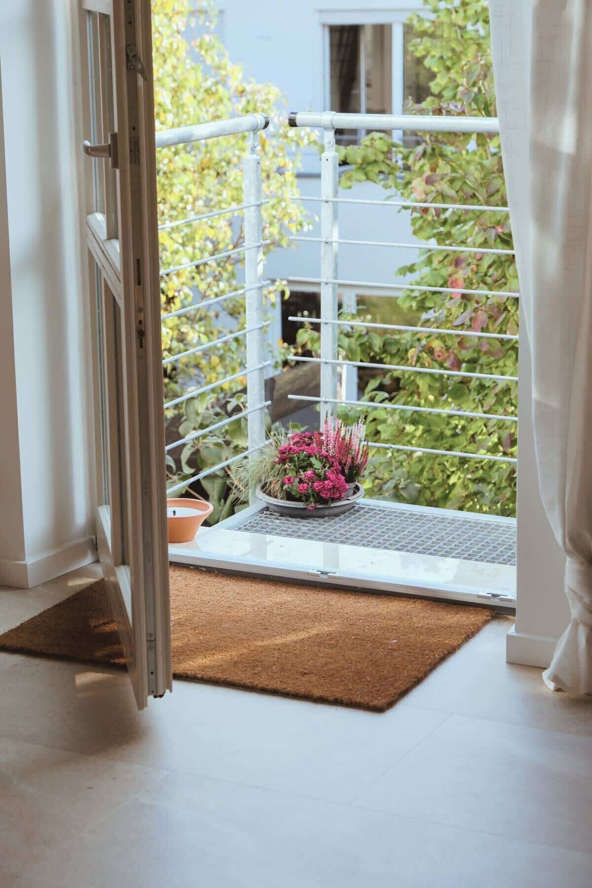 Ein Balkon mit Metallgeländer, einem Blumentopf und einer Fußmatte.