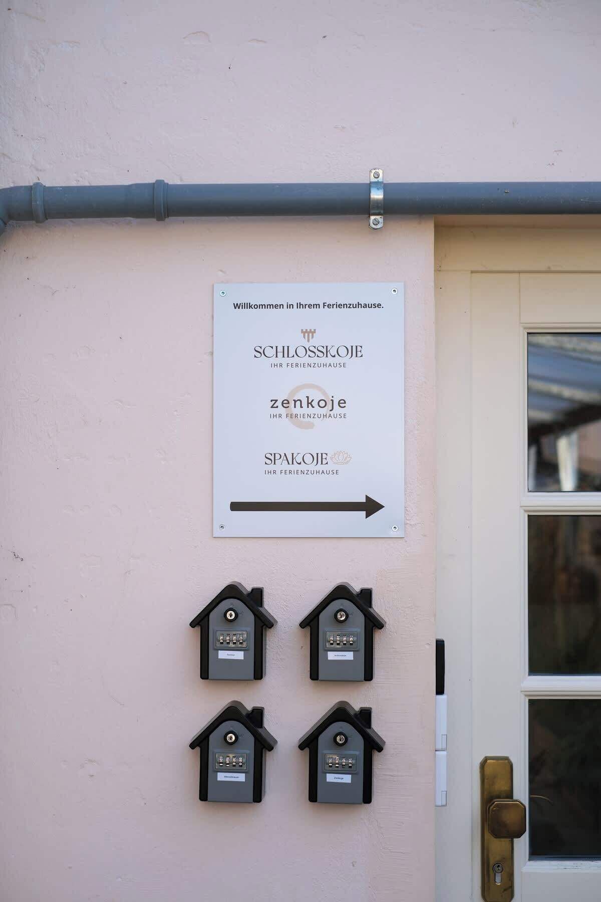 A sign with German text welcoming guests to a spa and wellness center, with directional arrows and four house-shaped mailboxes below.