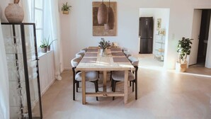 Uma área de refeições com uma mesa de madeira, cadeiras, luminárias pendentes e plantas em vasos.