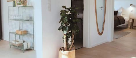 A living room with a potted plant, a wire shelf, and a large mirror.