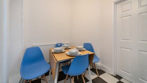 Un'area pranzo con un tavolo apparecchiato per quattro persone, sedie blu e una porta bianca sullo sfondo.