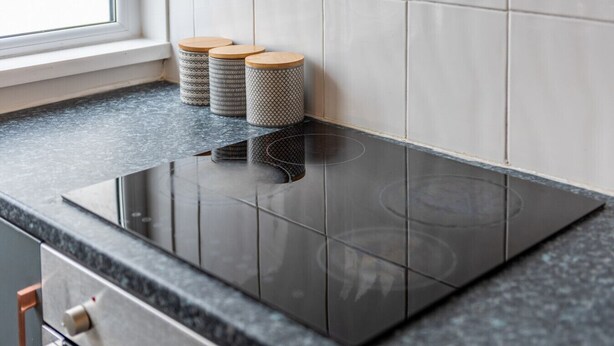 Una cucina con un piano cottura a induzione nero, tre contenitori decorati e una finestra.