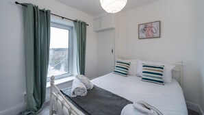 Una camera da letto con un letto, una finestra con tende, un comodino, una lampada e un quadro appeso al muro.