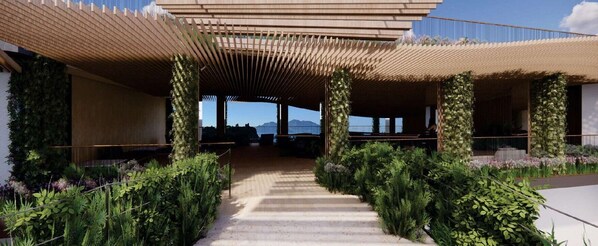 A covered outdoor area with a pathway leading to a building, surrounded by greenery and plants.