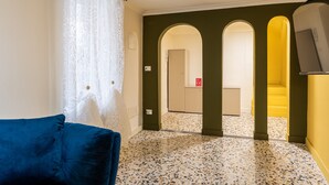 A room with a blue sofa, a patterned curtain, a tiled floor, and a hallway leading to a staircase. - Ortigia in Giallo by Wonderful Italy (Siracusa)