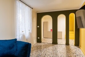 A room with a blue sofa, a patterned curtain, a tiled floor, and a hallway leading to a staircase. - Ortigia in Giallo by Wonderful Italy (Siracusa)