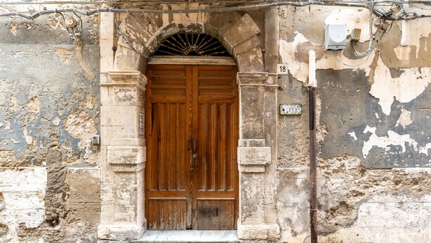 A weathered wooden door with a stone archway, a utility box, and a number plate. - Ortigia in Giallo by Wonderful Italy (Siracusa)