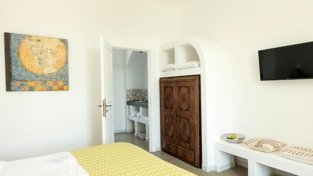 A bedroom with a bed, a wardrobe, a television, and a bathroom visible through an open door.