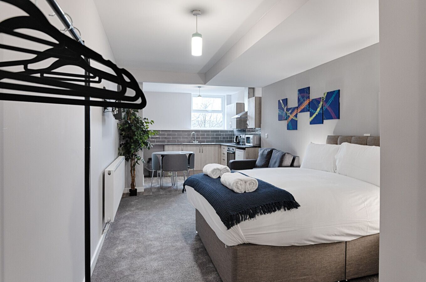 A modern hotel room with a bed, a small kitchenette, a dining area, and a view of the outside.