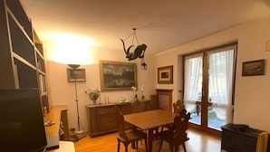 A living room with a wooden dining table, chairs, a TV, and a fireplace. - Casa Verocai Classic Retreat in Cortina (Cortina d'Ampezzo)